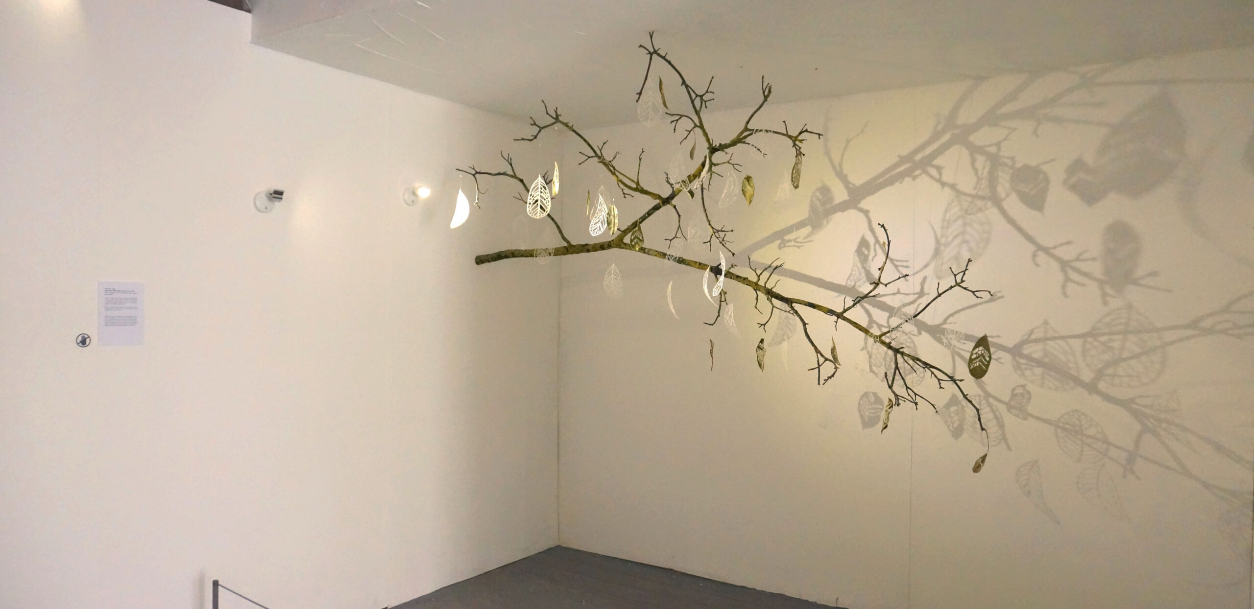 A mixed-media art installation made of carved leaves, glass leaves and a tree branch