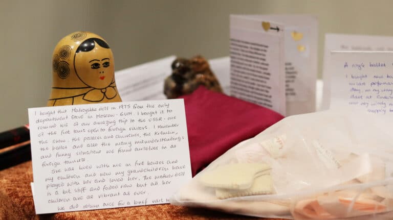 A selection of paper cards with handwritten text placed alongside some personal items, including ballet shoes and a Russian doll