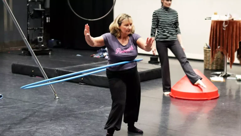 A middle-aged lady spinning a large, blue hula hoop on her waist