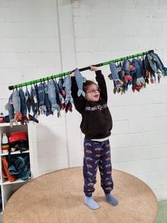 A smiling child holding up a green stick above her shoulders with many denim fish attached to it