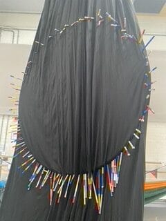 A black piece of hammock with a ring of colourful sticks attached to its front